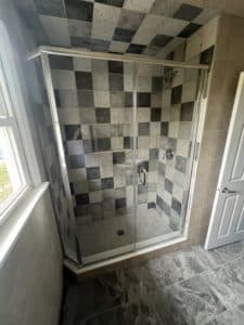 A shower area with a checkered-like wall and grey, ceramic flooring. 