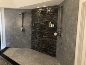 A shower with a textured, tile floor and dark, granite walls.