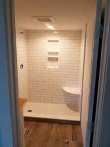 Walk-in shower with white subway tile walls, built-in shelves, and a corner bench, paired with a wood-look tile bathroom floor for a warm and modern aesthetic.