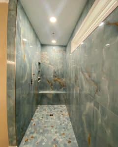 Luxurious shower with aqua blue marble-like walls and matching hexagonal tile floor, featuring warm golden veining and built-in shelving.