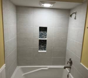 Bathtub shower with large format light gray tiles and a built-in niche featuring decorative blue mosaic tiles.